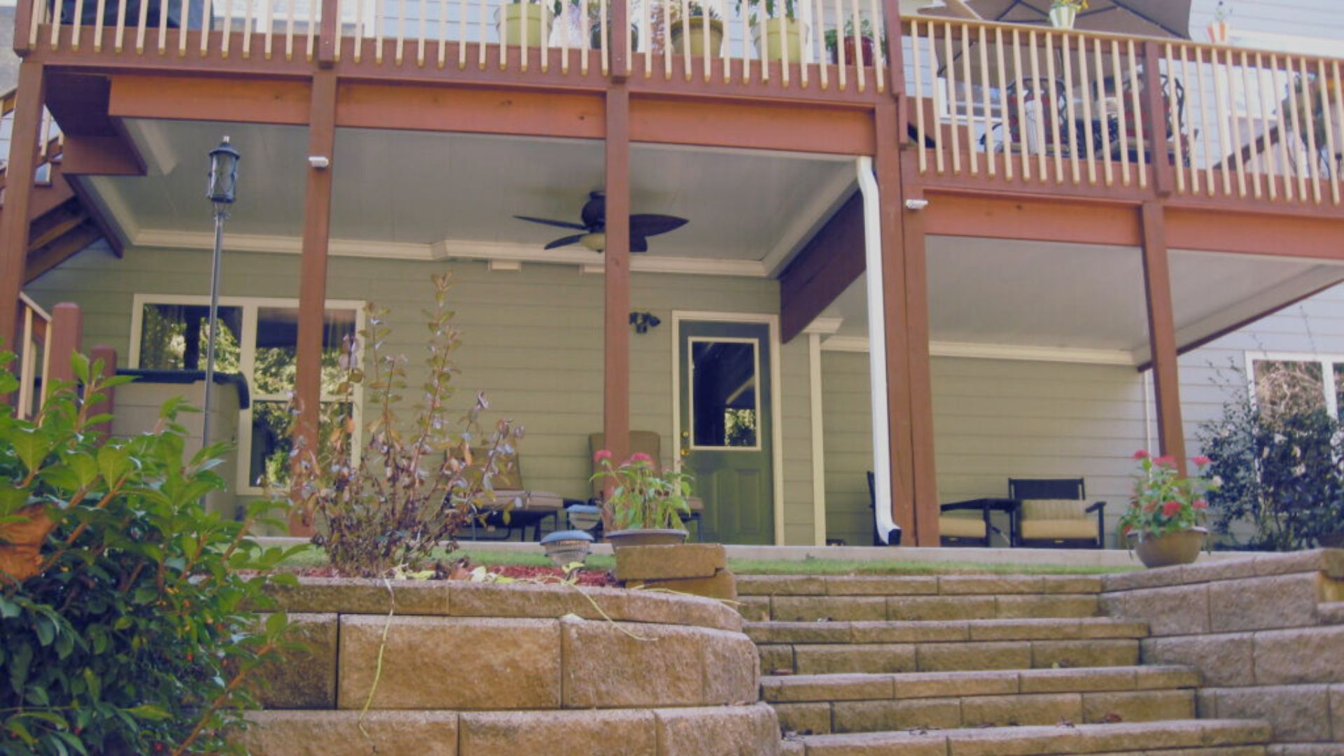 A wooden deck with stairs leading up to a house, surrounded by greenery and sunlight.