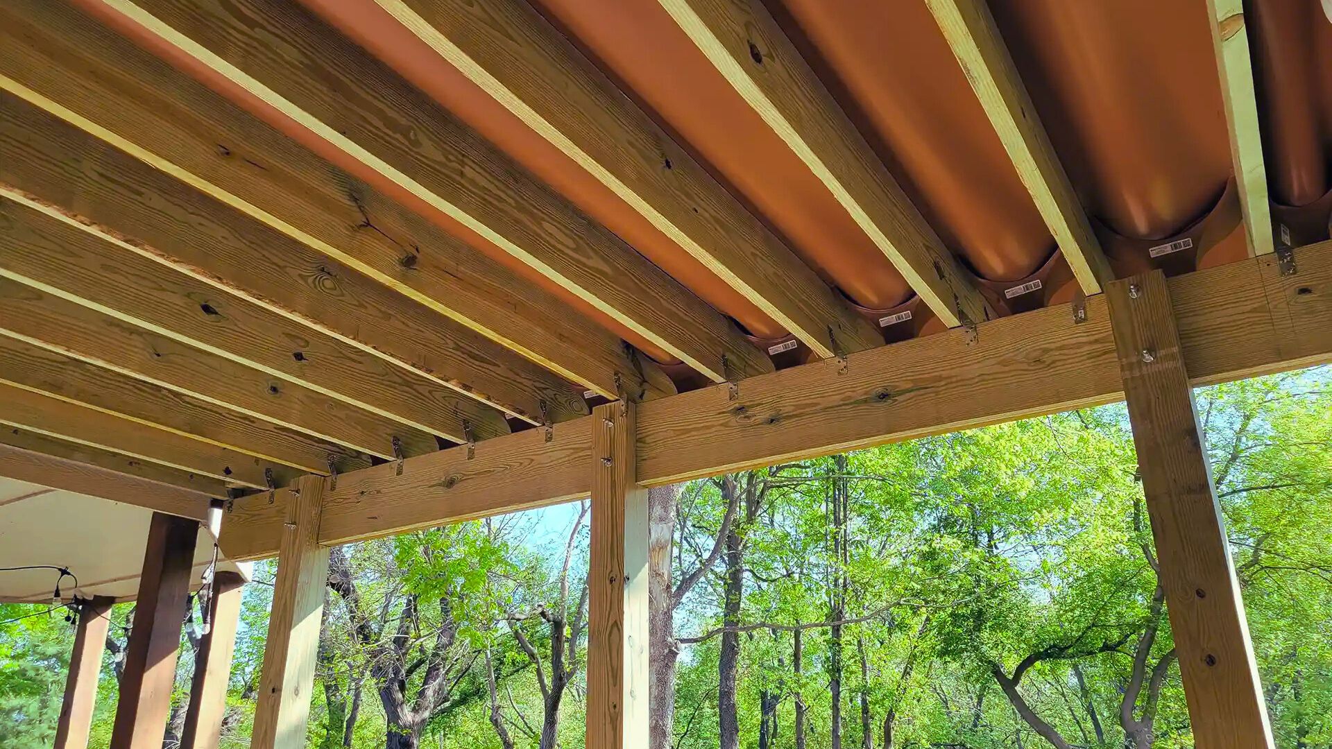 A covered porch featuring wooden beams and a table, creating a cozy outdoor seating area.