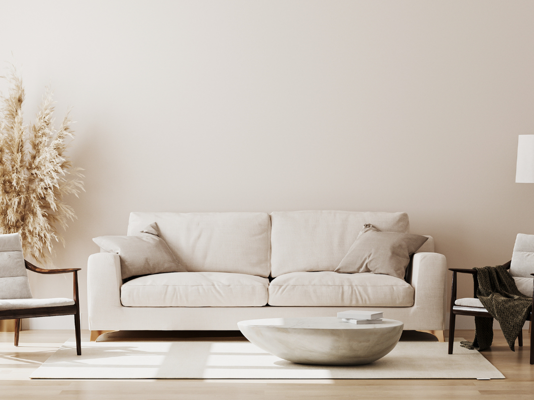 Minimalist living room with a beige sofa, two armchairs, and a round coffee table on a rug. Dried pampas grass adds a natural touch to the decor.