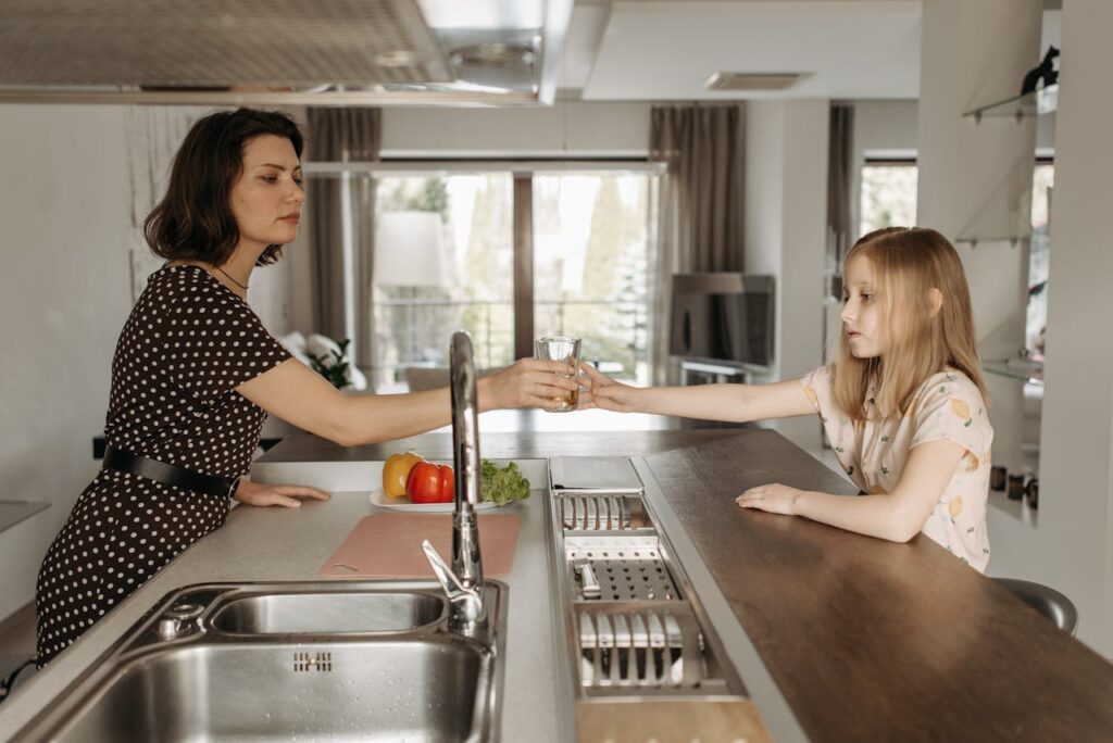 A woman and a young girl shake hands in a bright kitchen, symbolizing friendship and connection.