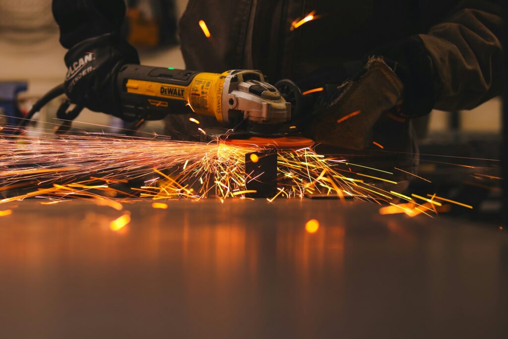How to Handle Metalwork Repairs Around Your Home Efficiently? A person using a metal grinder, sparks flying as they shape the metal piece in a workshop setting.
