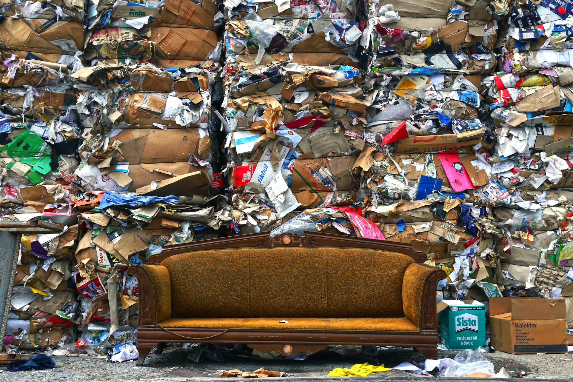 A couch positioned in front of a large pile of trash, highlighting a stark contrast between comfort and neglect.
