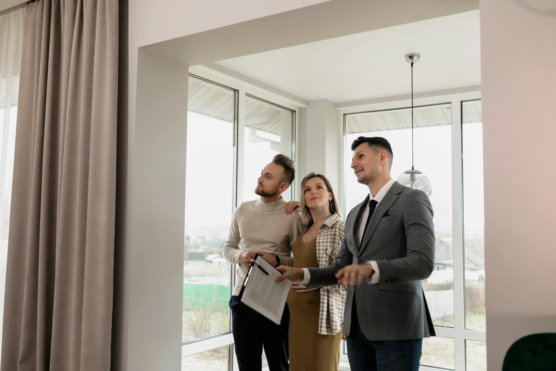 A trio of individuals stands in front of a window, looking intently at a house beyond.